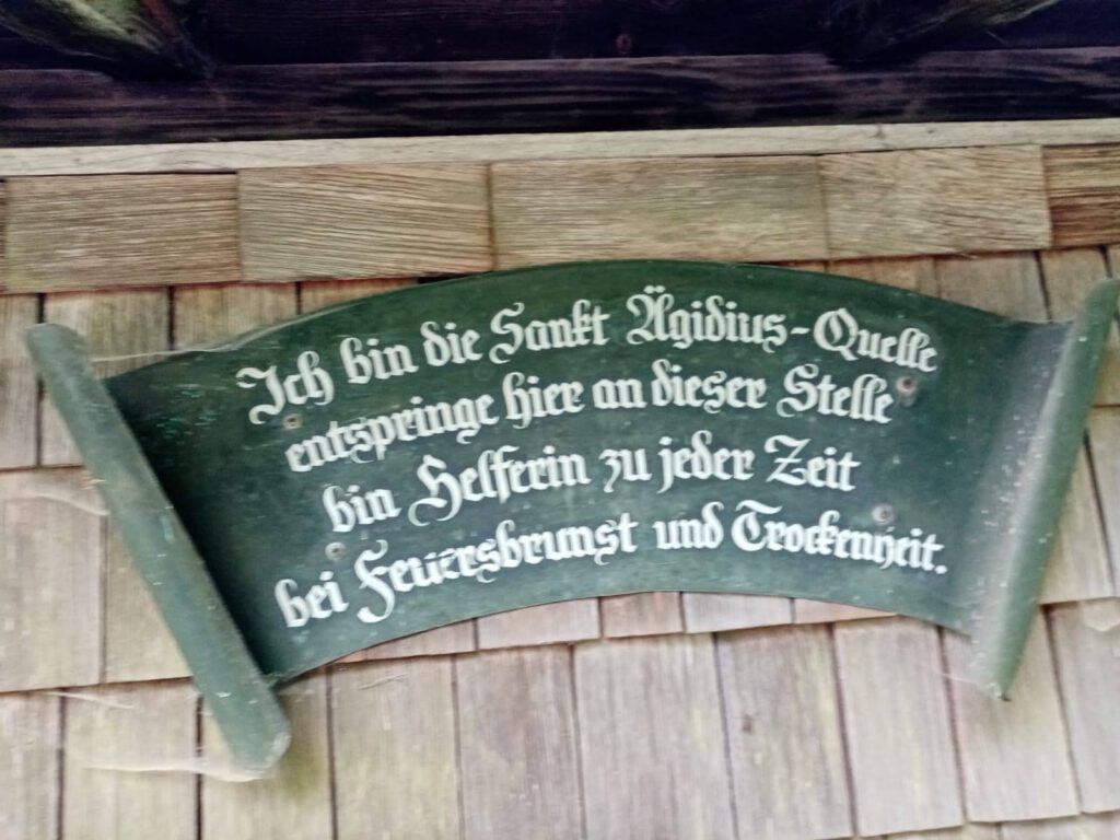 Text auf dem Schild, das an der Ägidius-Quelle Bergen hängt: Ich bin die Sankt Ägidius-Quelle, entspringe hier an dieser Stelle, bin Helferin zu jeder Zeit, bei Feuersbrunst und Trockenheit.