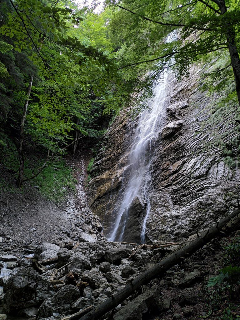 Auf dem Bild zu sehen ist ein kleiner Wasserfall, der eine hohe Felsmauer herunter fällt. 